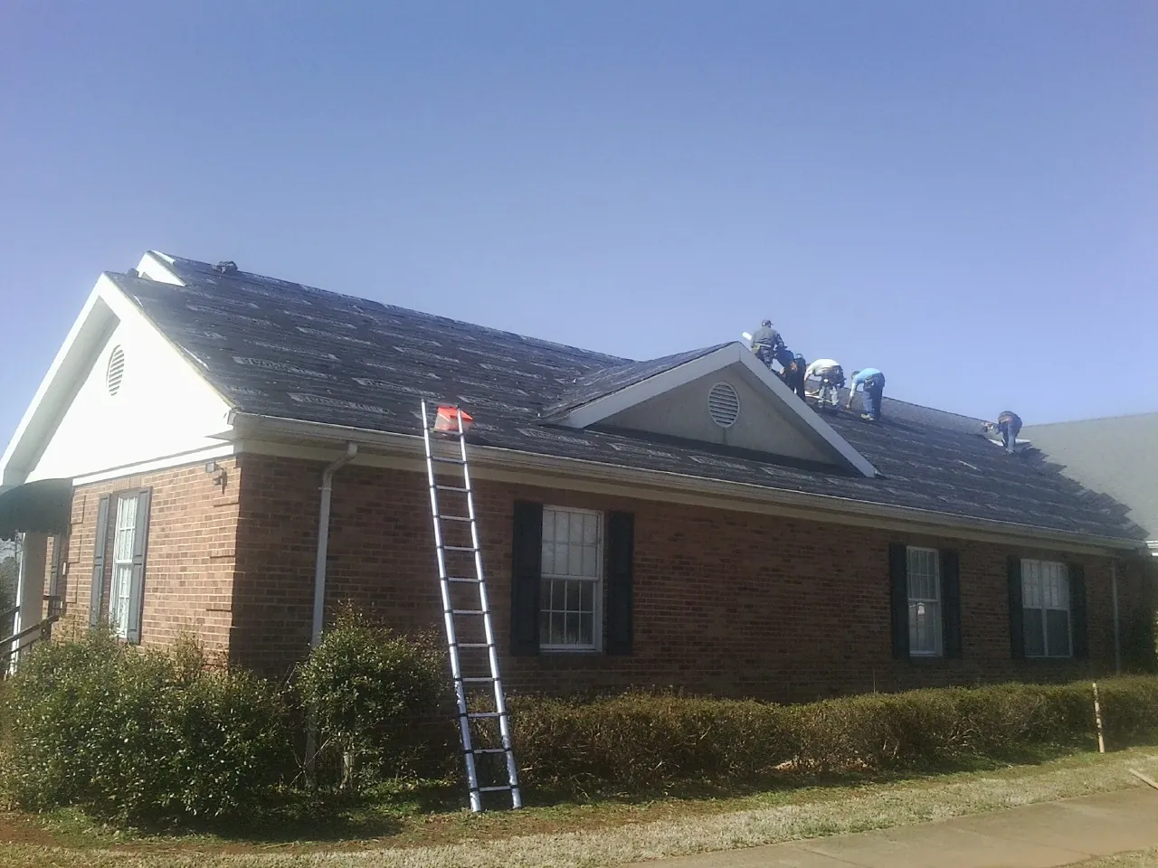 Crew tearing shingles off a brick ranch roof with a ladder set — Metal Roof Repair work by our crew in Hardin
