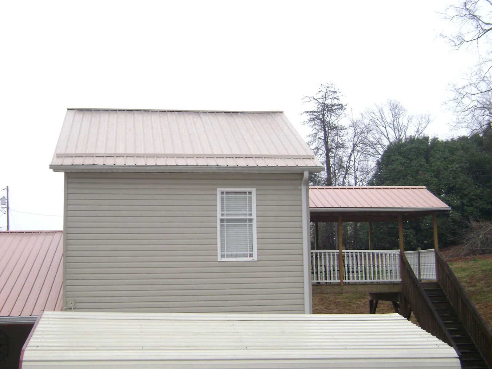 Tan metal roofs on a two story addition and attached porch, from a Roof Replacement job in Hardin